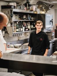 Junger Koch im Hotel Adler lächelt in der Küche.