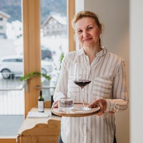 Freundliche Mitarbeiterin serviert mit einem Lächeln ein Glas Wein und Wasser im Hotelrestaurant.