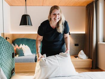 Mitarbeiterin beim Bettenmachen mit einem Lächeln im modernen Zimmer.