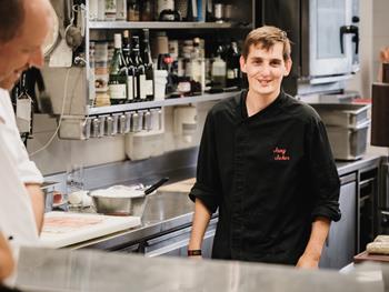 Hier wird Teamwork großgeschrieben Junger Koch im Hotel Adler lächelt in der Küche.