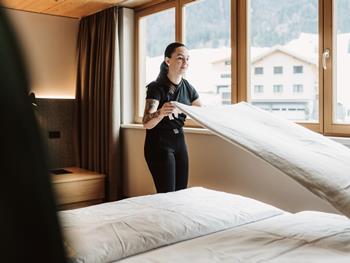 Mitarbeiterin beim Bettenmachen in einem hellen Zimmer mit Ausblick auf den verschneiten Bregenzerwald.