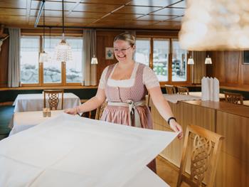 Dein Sprungbrett in die Welt des Tourismus Lächelnde Servicemitarbeiterin in Tracht beim Eindecken eines Tisches im Hotel Adler.