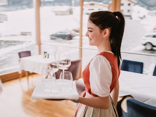 Junge Servicemitarbeiterin im Dirndl trägt Gläser im Hotel Adler.